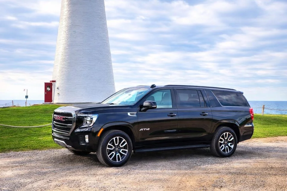 A black SUV parked beside a white lighthouse on the north shore