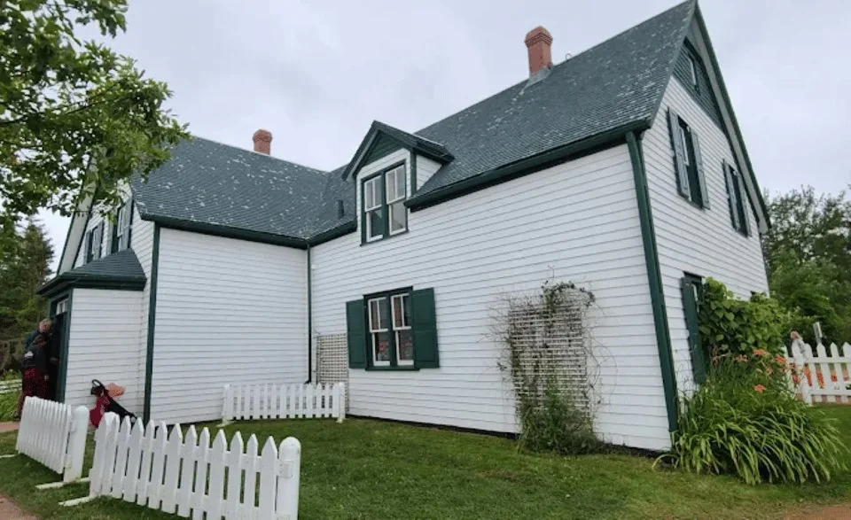 The white Green Gables farmhouse with green trim and gables, seen from the lawn